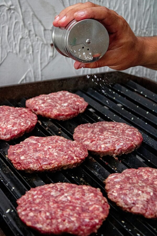 Close-up of beef patties being seasoned on a grill, ready for a delicious barbecue.