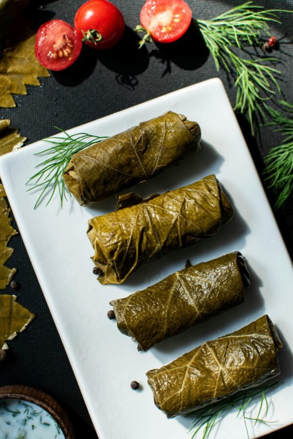 Appetizing dolma wrapped in grape leaves served with dill and cherry tomatoes.