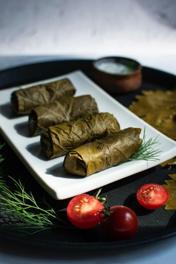 Close-up of traditional stuffed grape leaves on a white plate with fresh herbs and tomatoes.