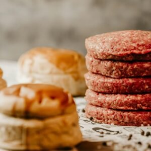 A stack of fresh raw beef patties with nearby burger buns, ready for cooking.